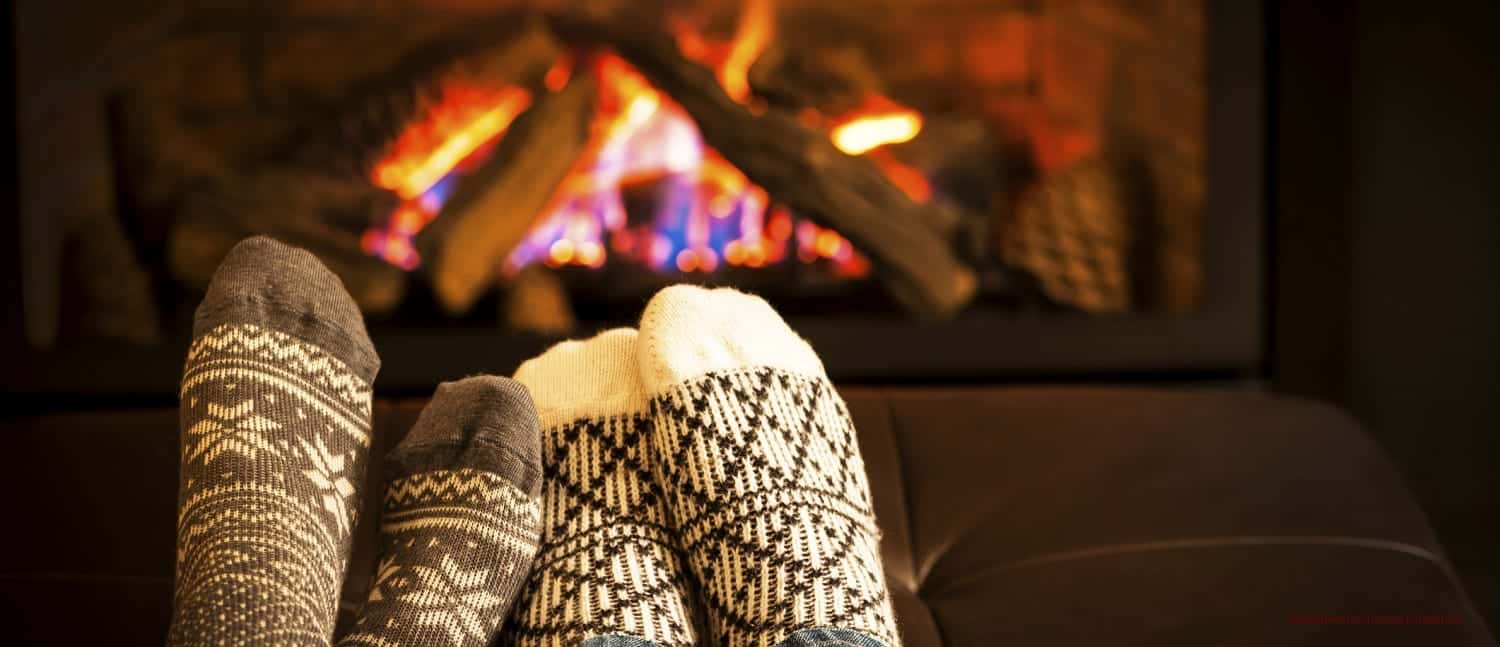 Two pairs of feet in cute knitted socks cozy up by the fireplace for a romantic evening.