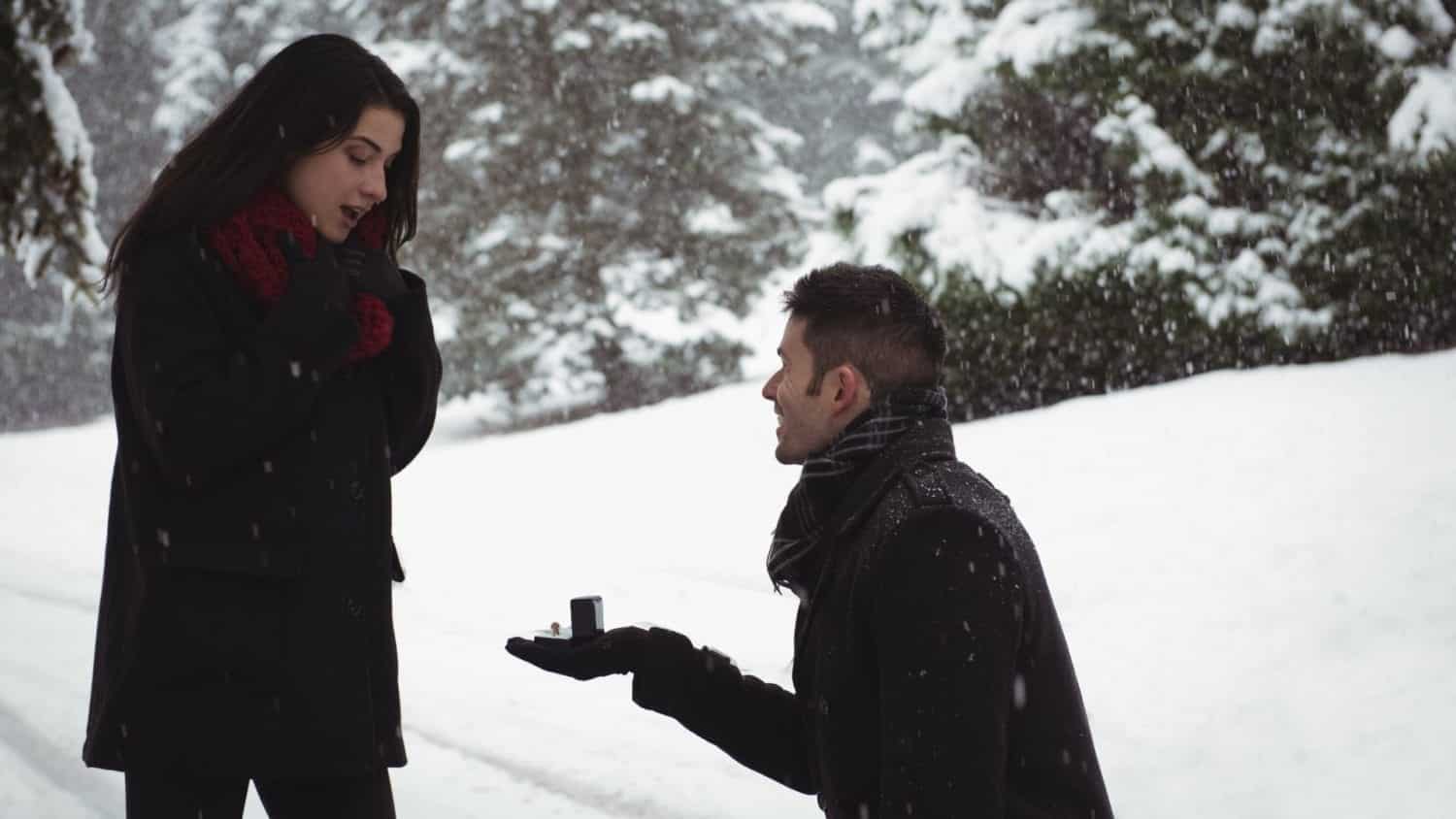 A man proposes to a woman in front of a snowy backdrop.