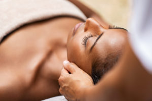 A massage therapist works on the head and neck muscles of a woman during a spa treatment.